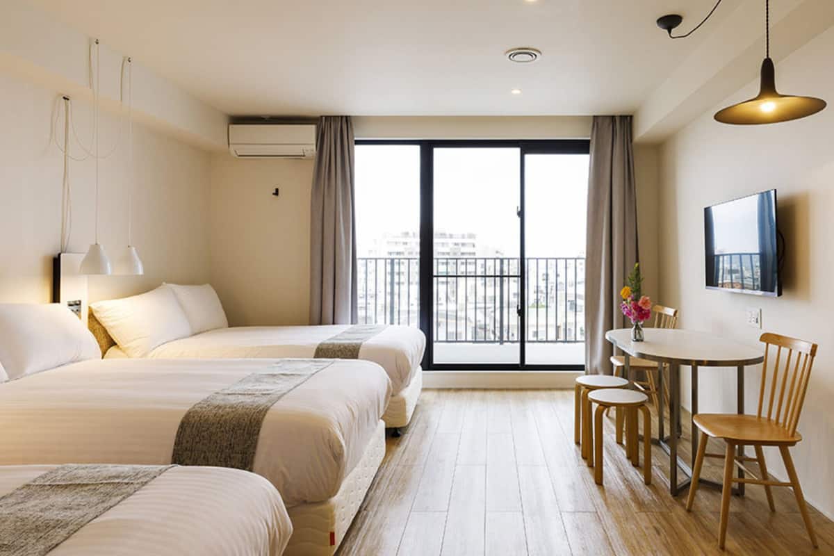 Une chambre d’hôtel avec deux lits, un coin repas comprenant une table et des chaises, un téléviseur fixé au mur et un balcon offrant une vue sur la ville.