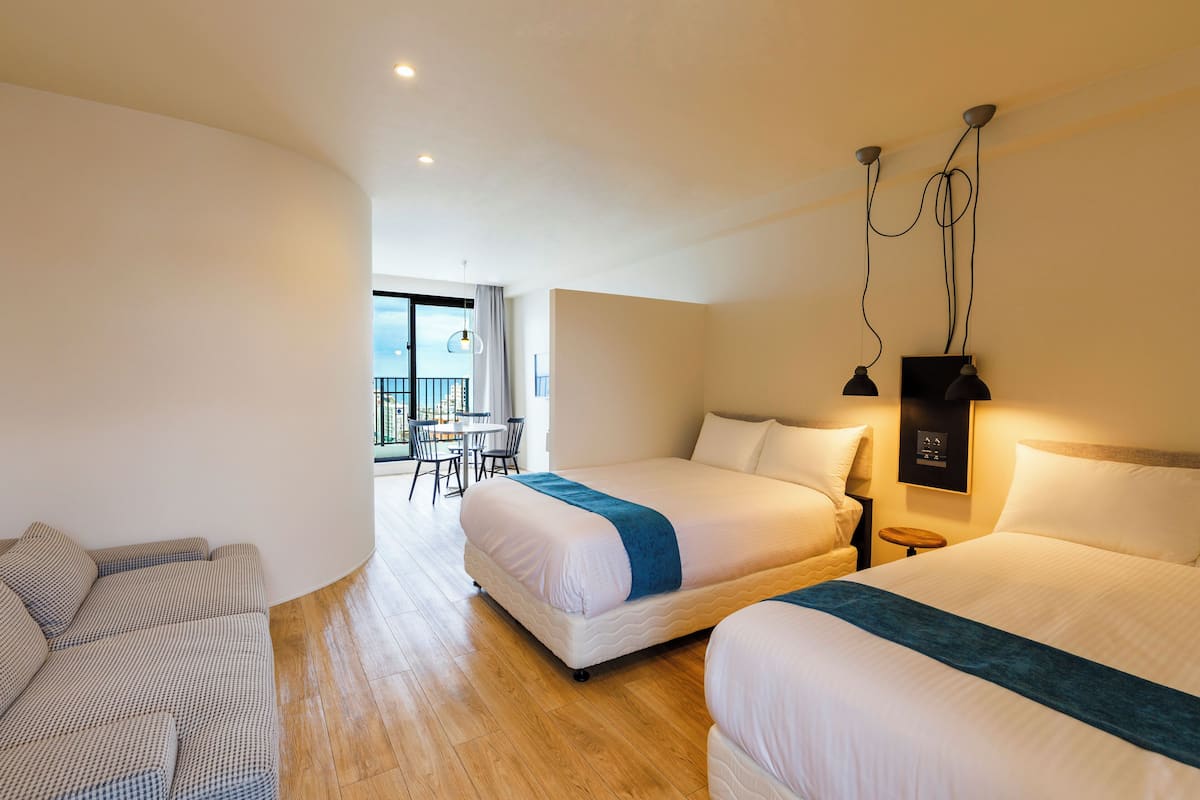 Une chambre d’hôtel avec deux lits, un canapé, une petite table et un balcon avec vue.