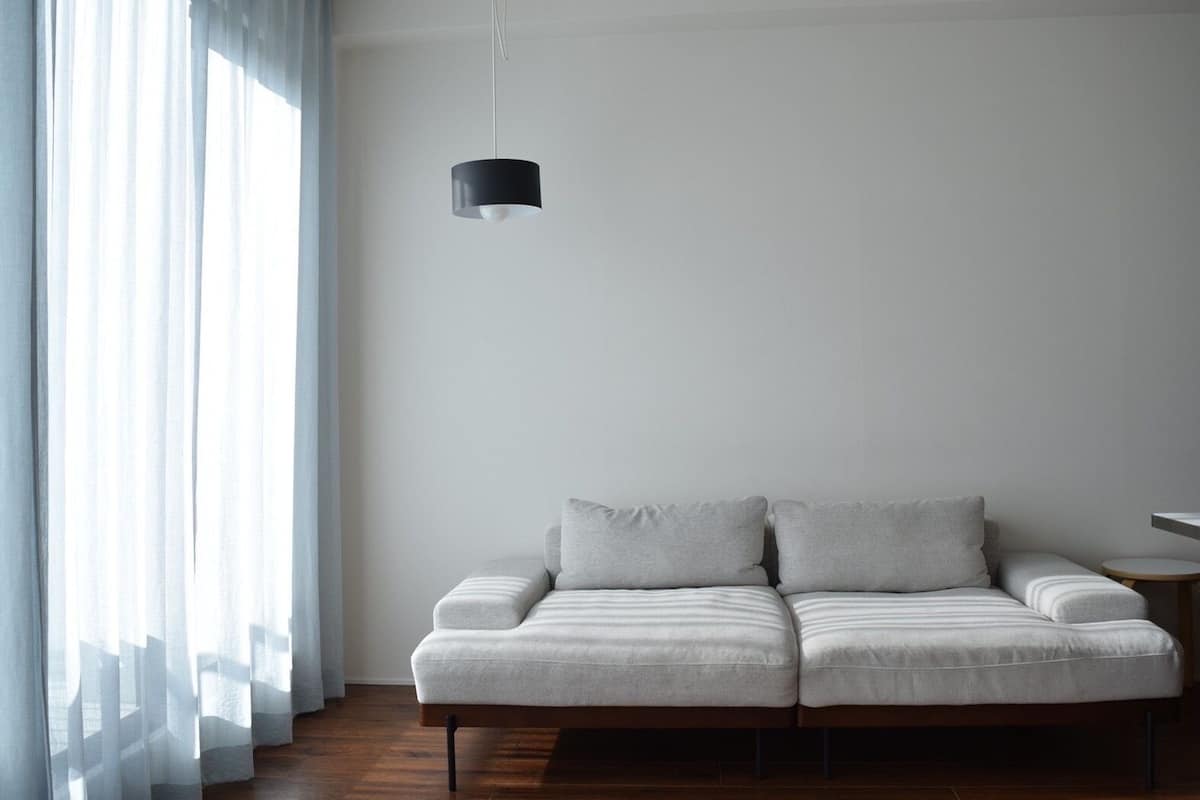 Un salon moderne avec un canapé, un luminaire suspendu et des rideaux légers.