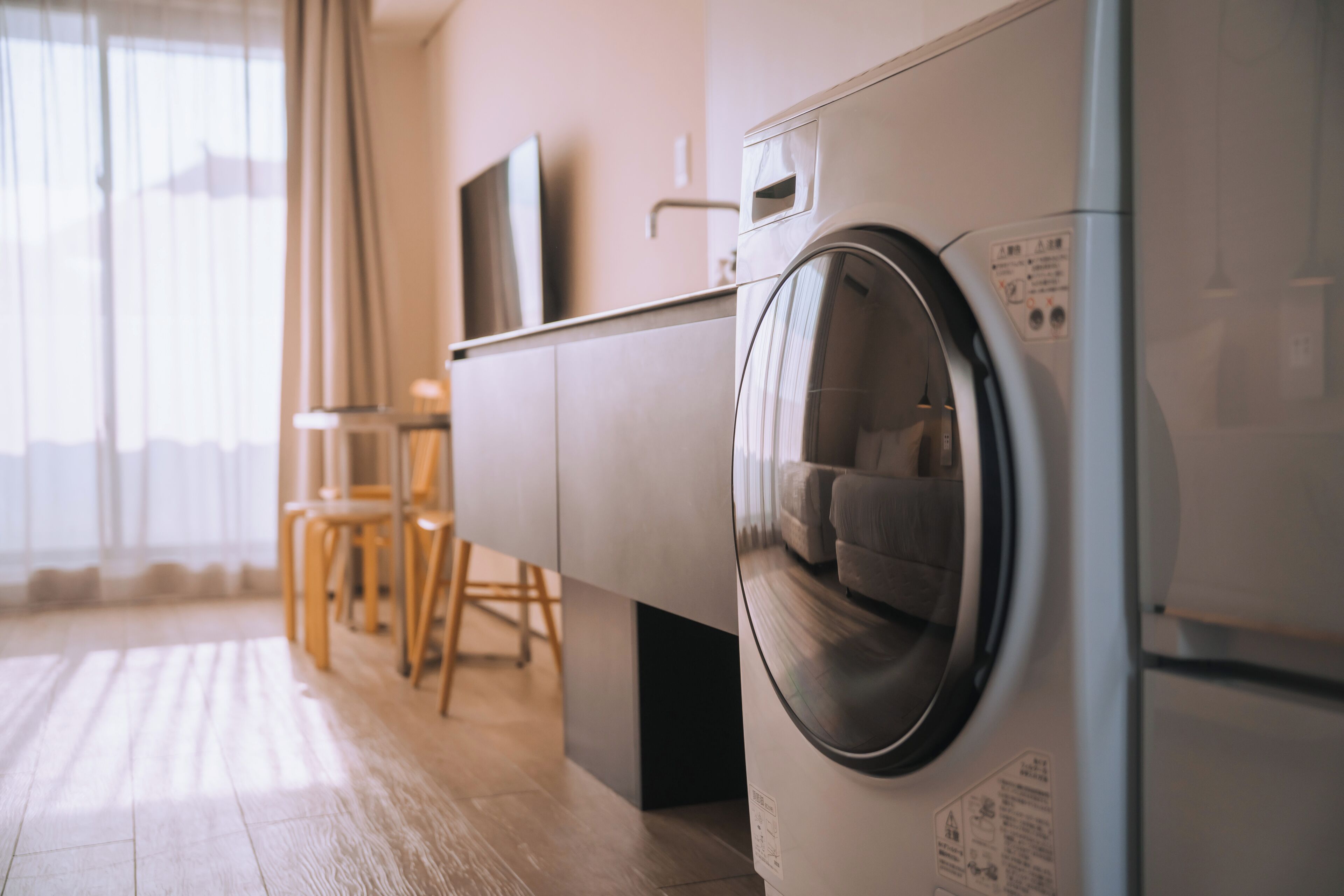 A modern laundry area with a washing machine, a television on a cabinet, and a dining area with chairs.