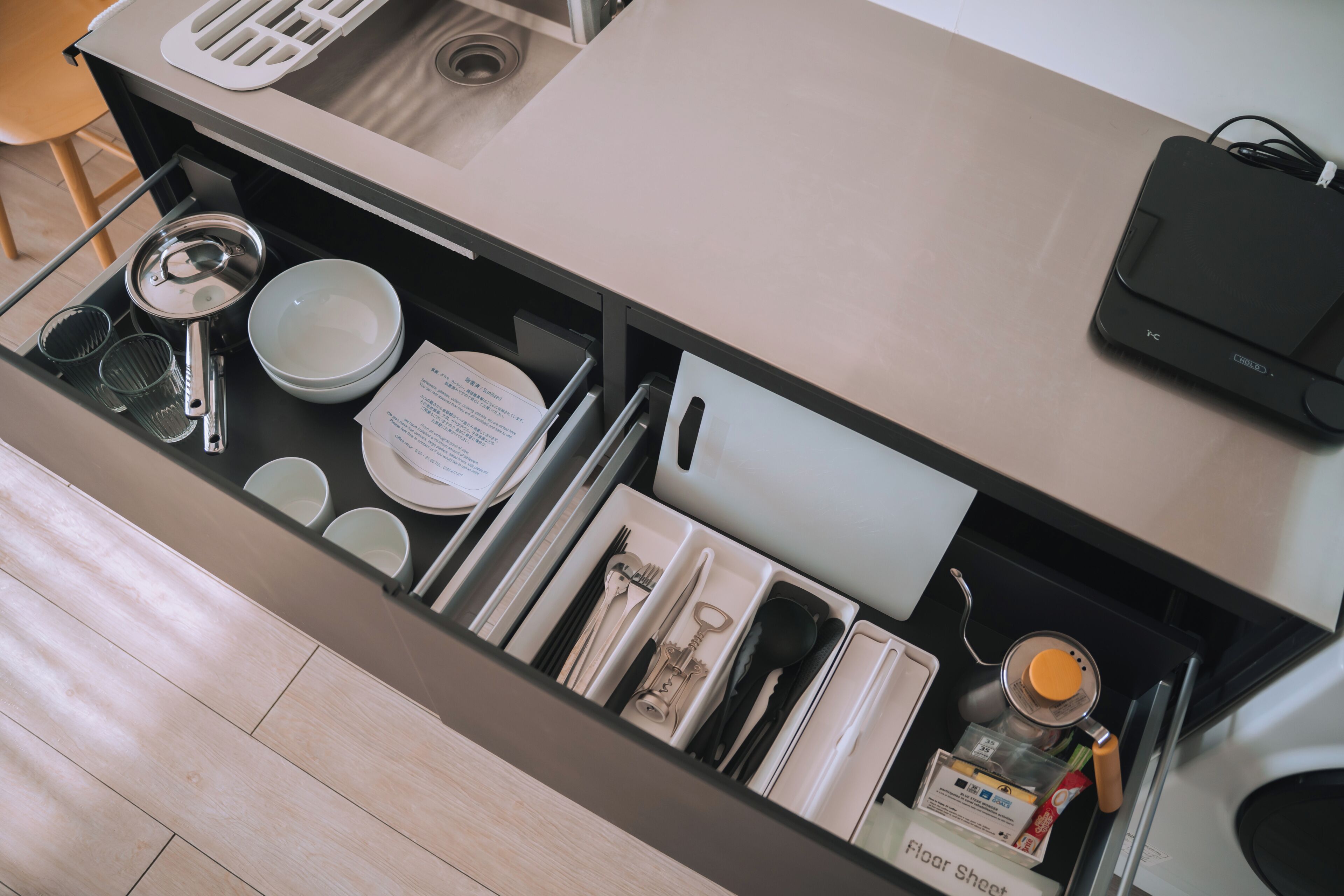 A kitchen drawer with utensils, plates, and a bottle of floor sheet.