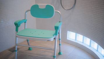A teal-colored child’s high chair in a bathroom with tiled walls and a shower.