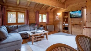 A wooden cabin interior with a sofa, a coffee table, a TV, and a staircase. - Chalet / Apartment Deluxe im Gartenhotel Rosenhof bei Kitzbühel (Oberndorf in Tirol)