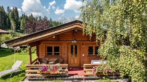 A wooden cabin with a porch, a bench, and a table with flowers. - Chalet / Apartment Deluxe im Gartenhotel Rosenhof bei Kitzbühel (Oberndorf in Tirol)