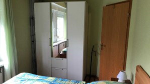 Quarto com cama, guarda-roupa, porta de madeira e mesa de cabeceira com abajur.