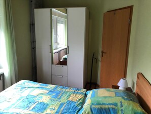 Makuuhuoneessa on sänky, vaatekaappi, puinen ovi ja yöpöytä, jossa on lamppu.