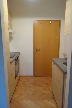 A compact kitchen with a wooden door, a built-in oven, and a countertop with a sink.