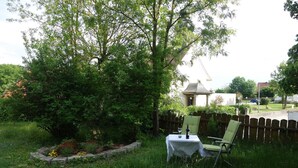 Um jardim com mesa e cadeiras, rodeado por vegetação e um cercado de madeira.