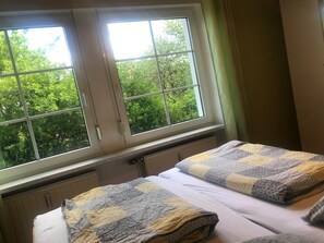 A bedroom with two beds, a window with a view of trees, and a radiator below the window. - Vacation apartment north-east (for 2 - 4 persons) - Ferienwohnungen May (Plankenfels)