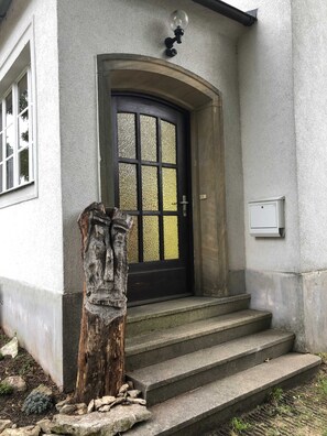 A house with a black door, a small porch, and a wooden sculpture. - Vacation apartment north-east (for 2 - 4 persons) - Ferienwohnungen May (Plankenfels)