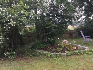 A garden with a wooden fence, a flower bed, and a folding chair. - Northeast Vacation Apartment (for 2–4 people) - Ferienwohnungen May (Plankenfels)