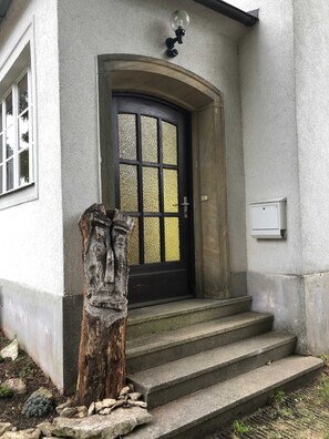 A house with a black door, a small porch, and a wooden sculpture.