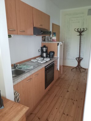 A compact kitchen with wooden cabinets, a built-in oven, a sink, and a coffee maker.