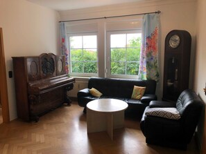 A living room with a piano, a sofa, a coffee table, and a clock on the wall.