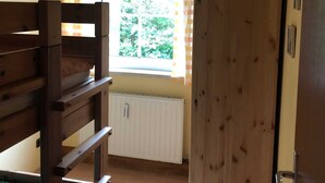 Um quarto com uma cama beliche, uma janela com cortinas, um radiador e uma porta de madeira.