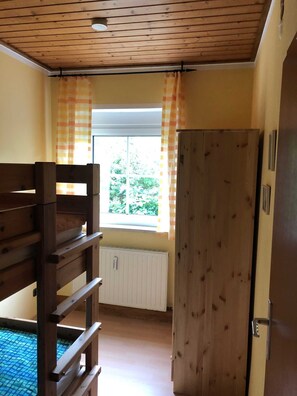 Huoneessa on kerrossänky, ikkunassa on verhot, siellä on patteri ja puinen ovi.