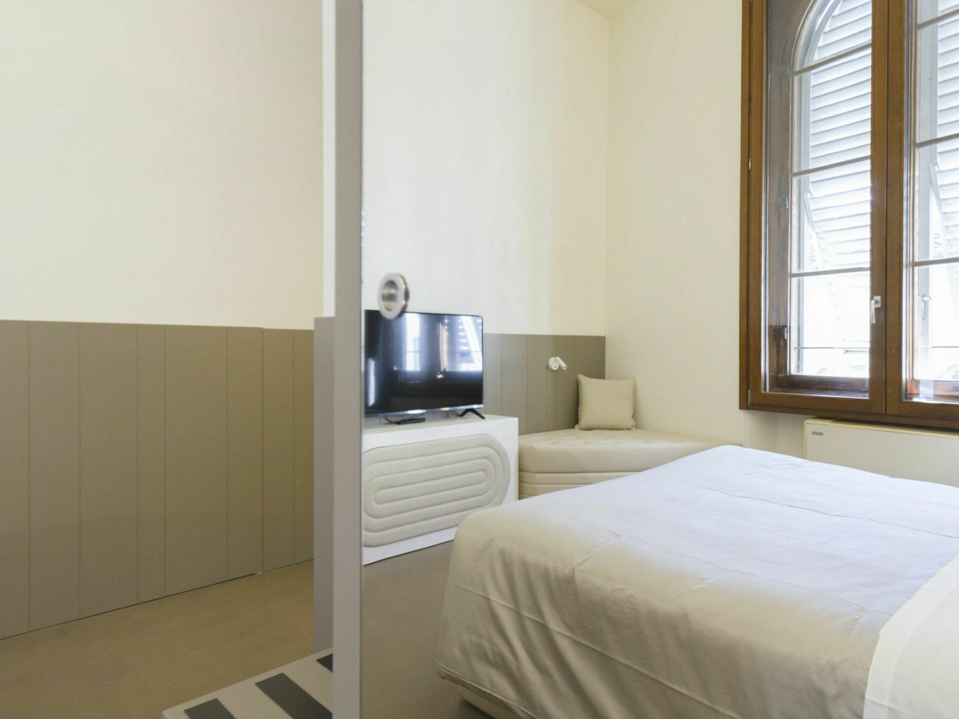 A hotel room with a bed, a television, a small seating area, and a window.