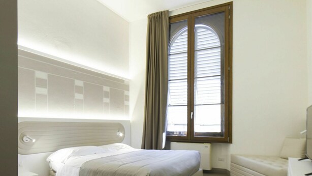 A modern hotel room with a large bed, a bedside table, a window with curtains, and a radiator. - Beautiful apartment for 5 guests with A/C, WIFI and TV (Florence)