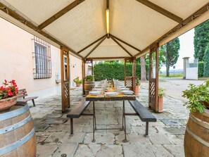 An outdoor dining area with a covered table set for a meal, surrounded by wooden benches and potted plants. - Stunning private villa for 20 people with WIFI, private pool, TV, patio and pets allowed (San Miniato)