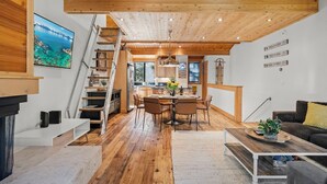 Ein großzügiger Wohnbereich mit Holzboden, einem Esstisch mit Stühlen, einer Couch, einem Couchtisch mit Pflanzen und einer Treppe, die in eine obere Etage führt.