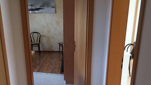 A hallway with wooden flooring leading to a room with a tiled floor. A painting is visible on the wall, and there are two chairs in the room. - Kleine Mietidee (Markranstaedt)