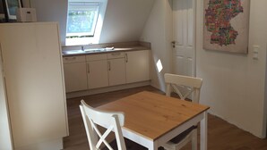 A compact kitchen with a window, a dining table, and a white chair. - Huus Windroos Wohnung 2 (Jemgum)