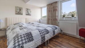 Una camera da letto con un letto grande, una finestra con tende, due quadri appesi al muro e un termosifone.