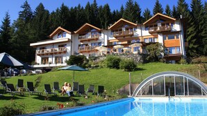 A hotel with multiple balconies, a swimming pool, and a lush green hillside. - Ferienwohnung Österreich im Gartenhotel Rosenhof bei Kitzbühel (Oberndorf in Tirol)