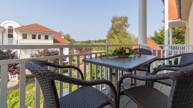 Ein Balkon mit Korbstühlen und einem Tisch, mit Blick auf ein Wohngebiet mit Häusern und Grünflächen.