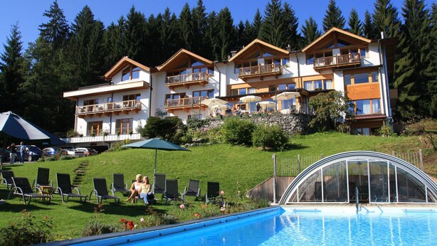 A hotel with multiple balconies, a swimming pool, and a lush green hillside. - Chalet Villa Rosa im Gartenhotel Rosenhof bei Kitzbühel (Oberndorf in Tirol)