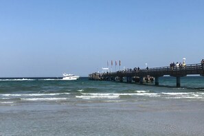 A pier extending into the ocean with a boat in the distance and people walking along it. - Ferienwohnung Witthus Han/806 (Scharbeutz)