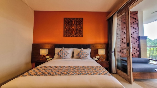 A hotel room with a large bed, two bedside tables with lamps, a decorative wall piece, and a balcony with a brick wall and blue seating. - Kahayana Suites (Ubud)