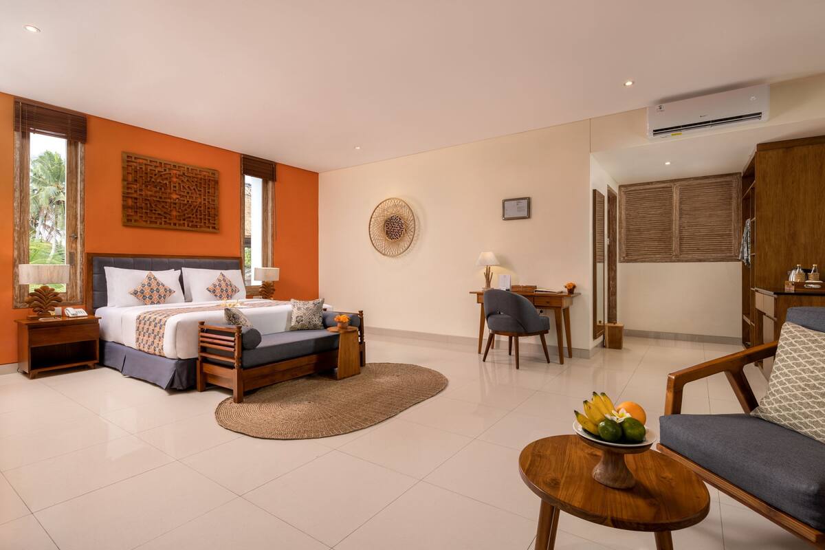 A bedroom with a bed, bedside tables, a desk, a chair, and a small table with fruit.