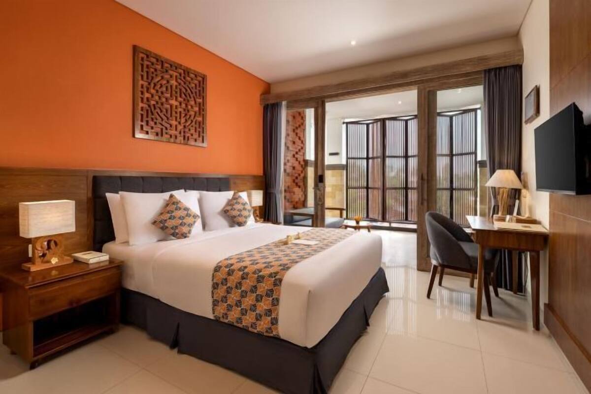 A hotel room with a large bed, a desk, a chair, a TV, and a view through the glass doors.
