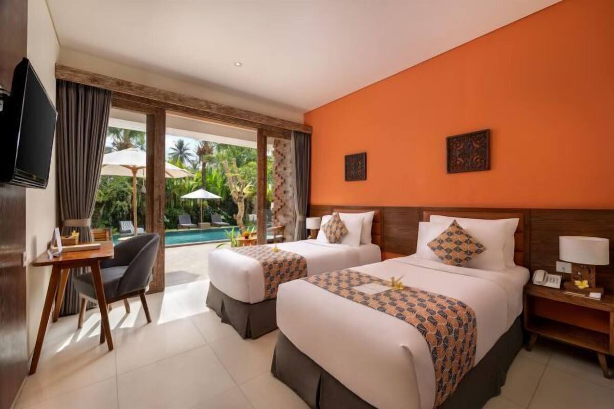 A hotel room with two beds, a desk, a chair, a TV, and a view of the pool.