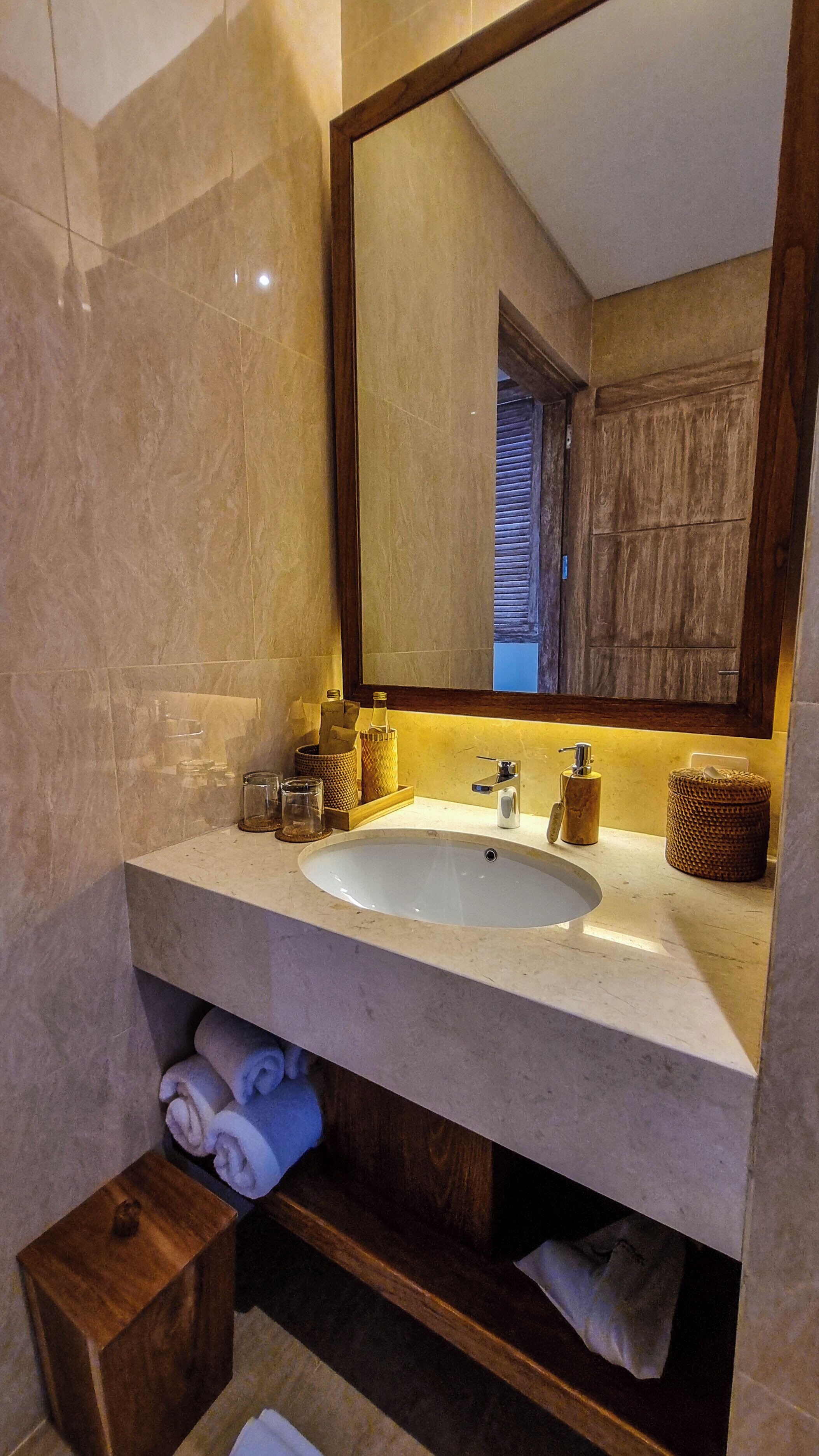 A bathroom with a large mirror, a sink, and a wooden shelf below.