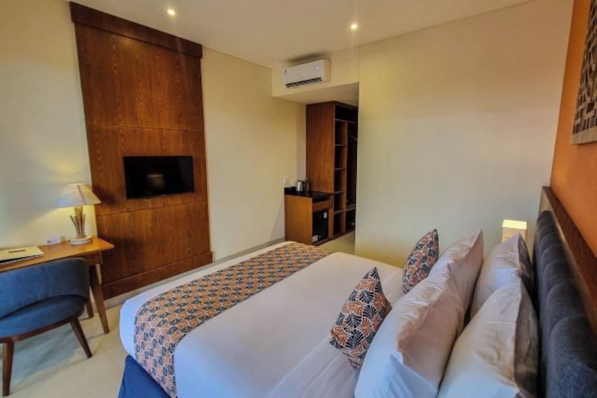 A hotel room with a bed, a desk, a TV mounted on the wall, and a wardrobe.