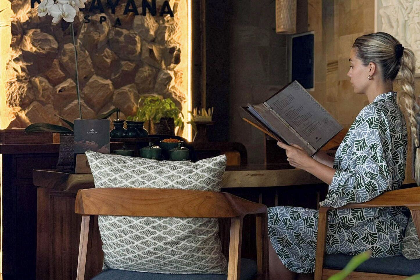 A person reading a menu in a cozy, well-lit room with a stone wall, wooden furniture, and decorative plants.