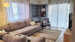 Una sala de estar con sofá, sillón, televisor y estantería.