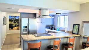 Cocina compacta con una isla central, electrodomésticos de acero inoxidable y un comedor con sillas de madera.