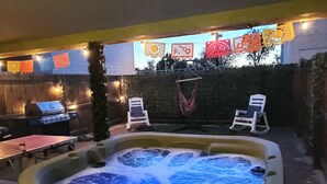 Un jacuzzi con pantalla digital, dos sillones de descanso, una parrilla de barbacoa y farolillos decorativos.