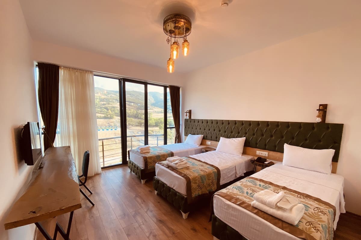 A hotel room with two beds, a desk, and a large window with a view of the countryside.