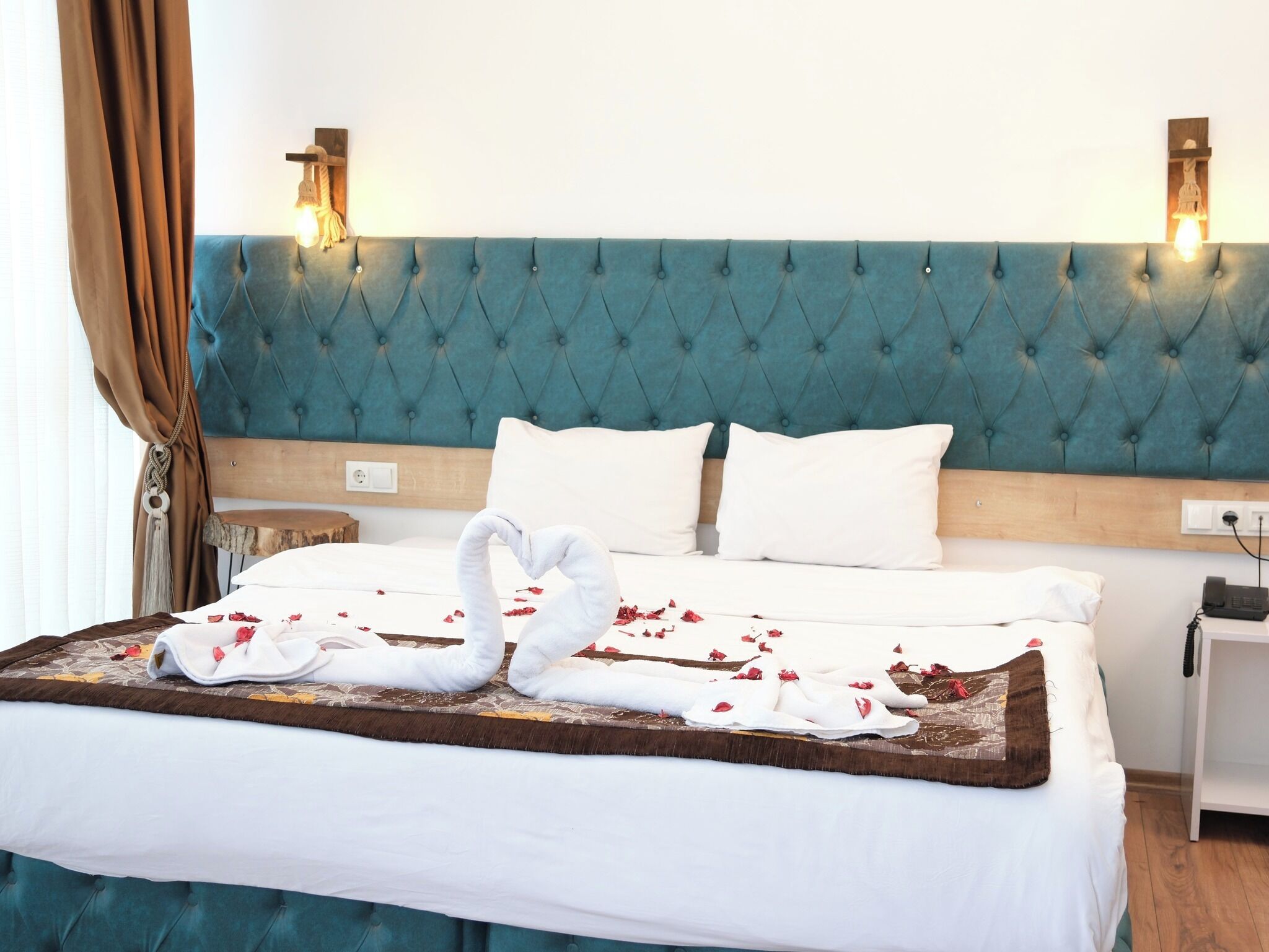 Ein Hotelzimmer mit einem rautenförmigen, türkisfarbenen Kopfteil, weißer Bettwäsche, einer Schwan-Form aus Handtüchern und einem Nachttisch aus Holz mit einem Telefon.