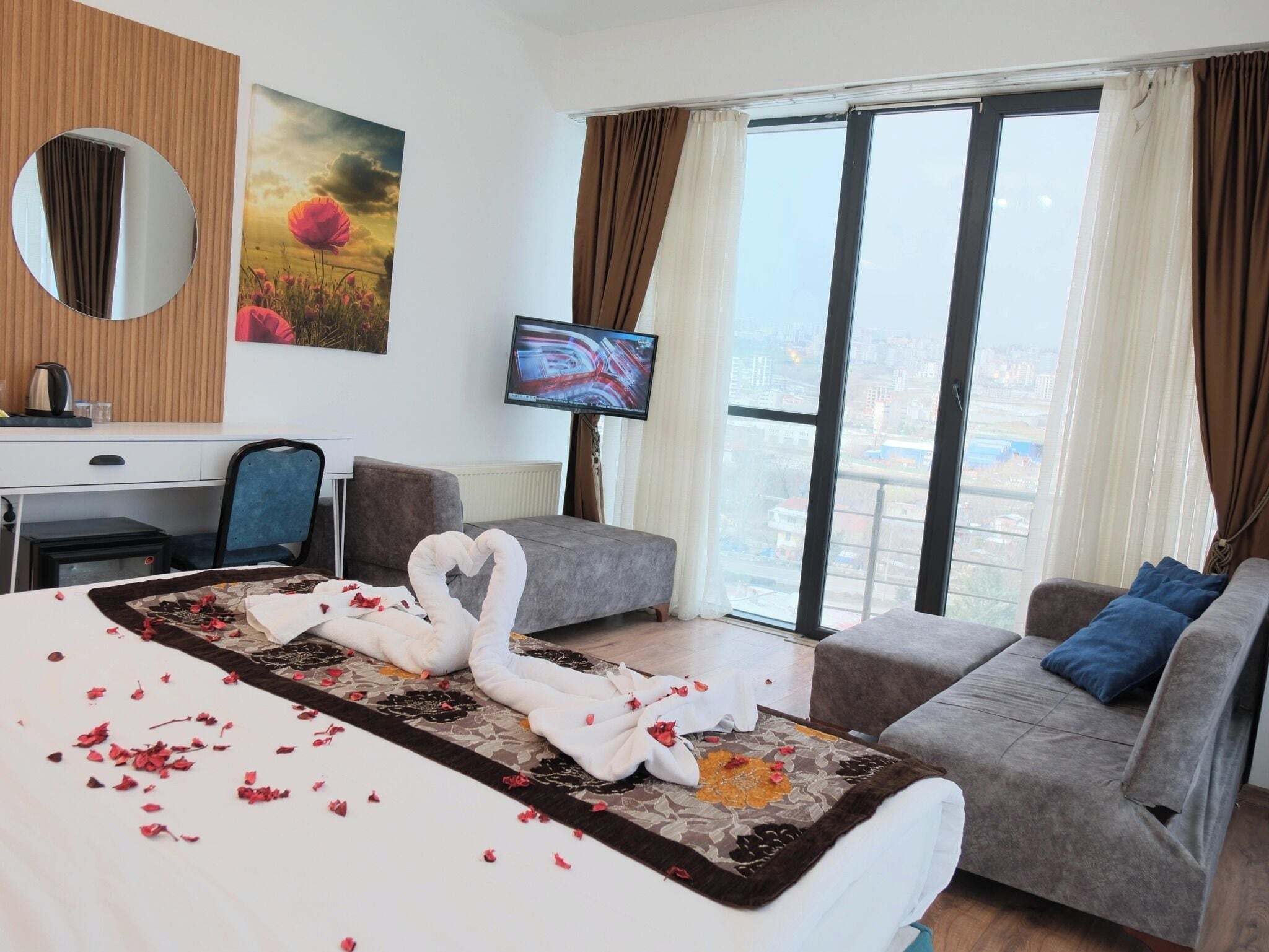 Ein Hotelzimmer mit Bett, Sofa, Fernseher, Schreibtisch und einem Fenster mit Blick auf die Stadt.