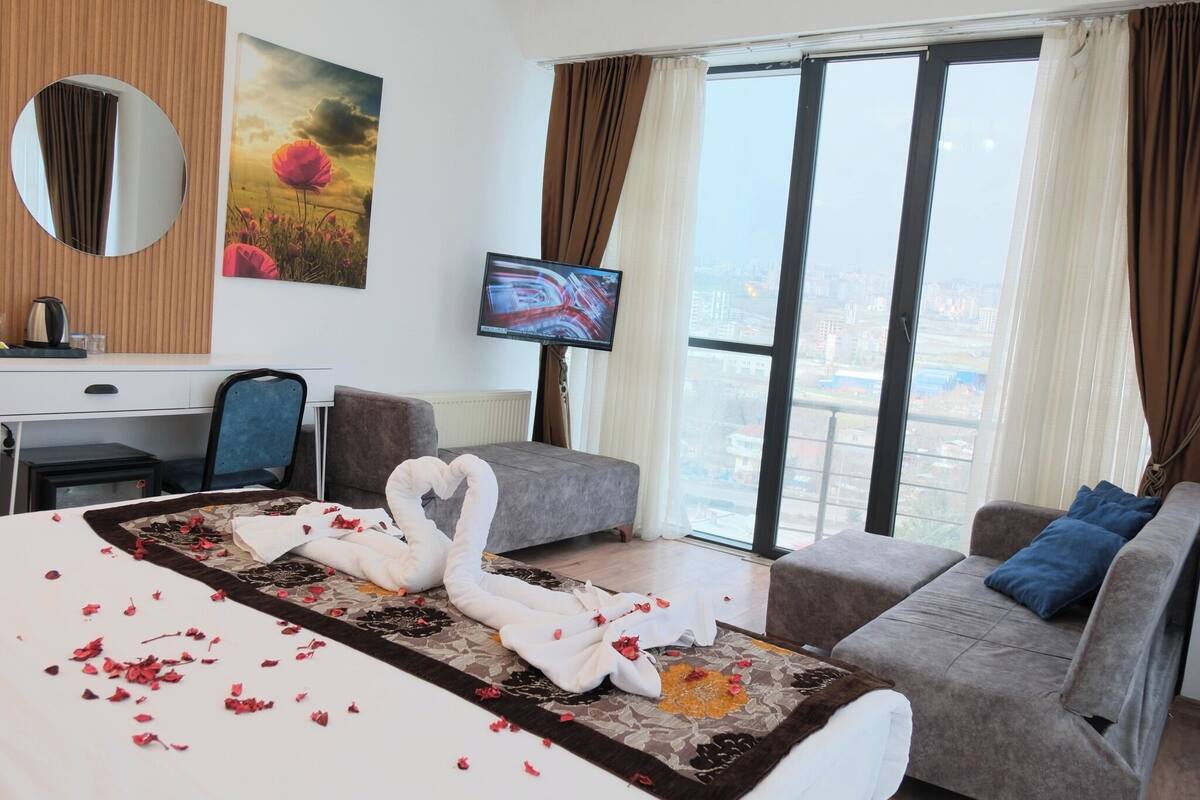 A hotel room with a bed, a sofa, a TV, a desk, and a window with a city view.