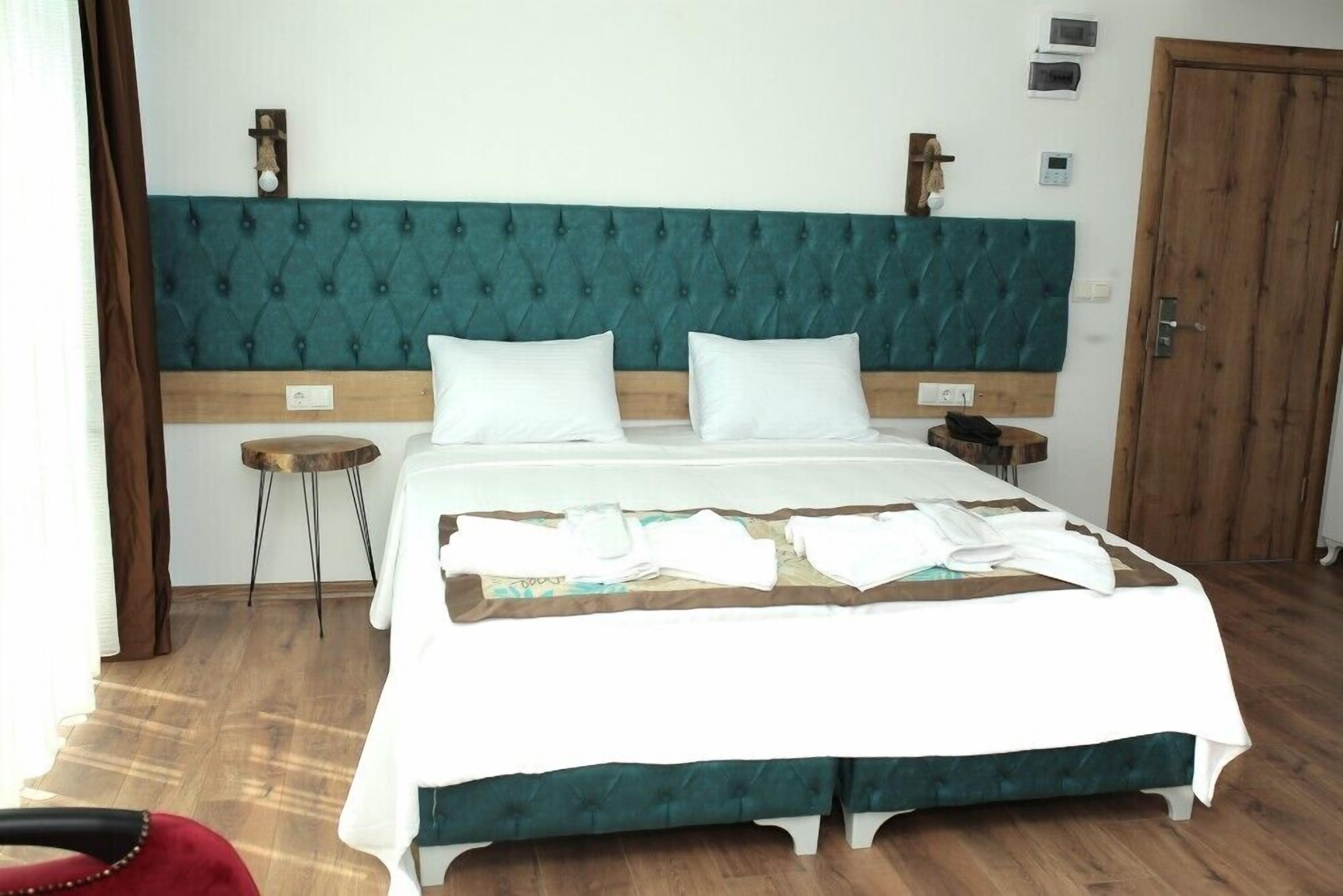 A neatly made bed with a teal headboard, a bedside table, and a wooden door in a hotel room.
