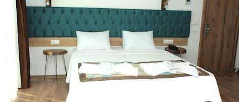 A neatly made bed with a teal headboard, a bedside table, and a wooden door in a hotel room.