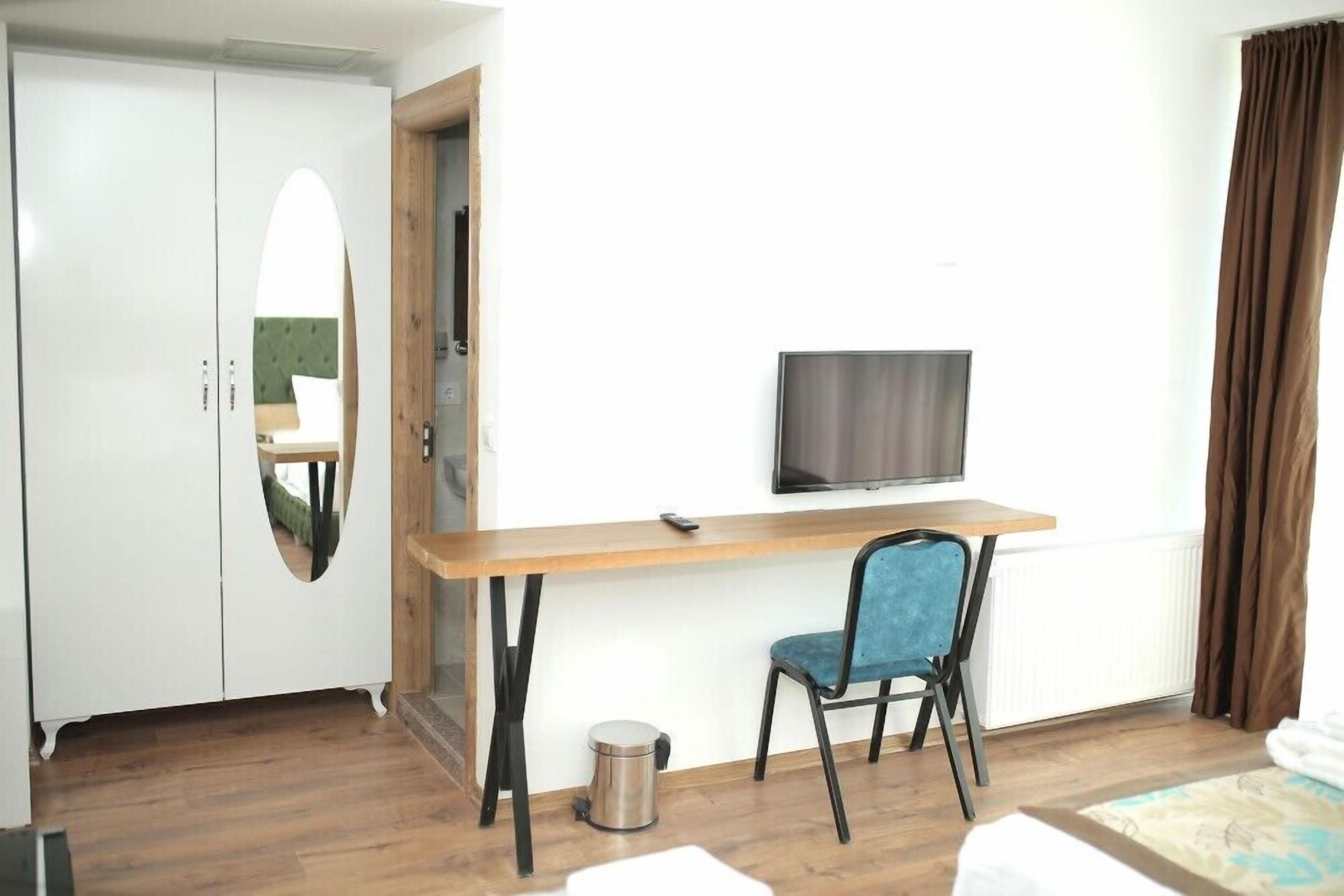 Una habitación con un escritorio de madera, una silla azul, televisor, armario y radiador.