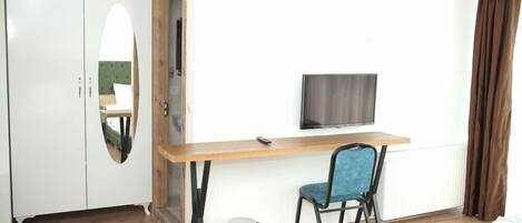 Una habitación con un escritorio de madera, una silla azul, televisor, armario y radiador.