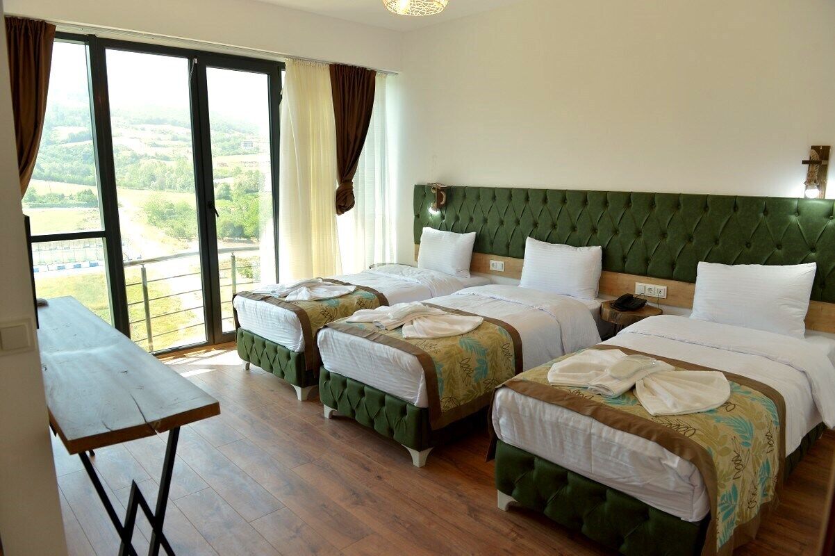 A hotel room with three beds, a wooden table, and a view of the countryside.